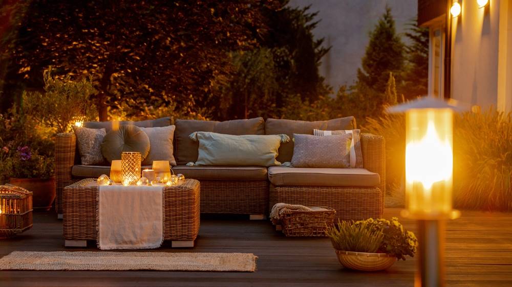 Wicker patio furniture with cushions and candles under evening lights