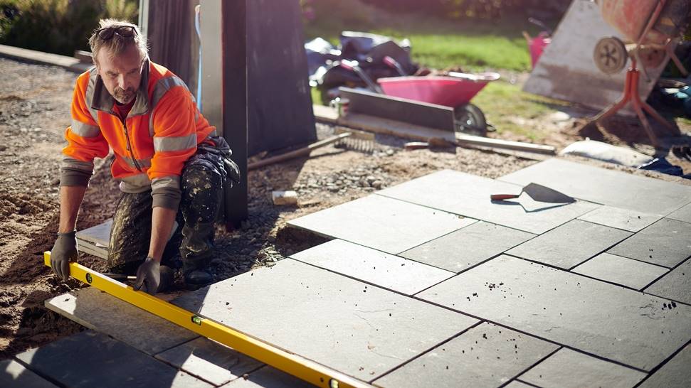 Worker using a level to install stone patio slabs in a garden