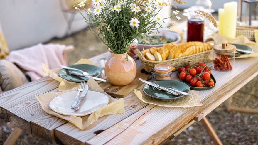 Outdoor patio dining setup with a rustic wooden table, fresh food, and daisies