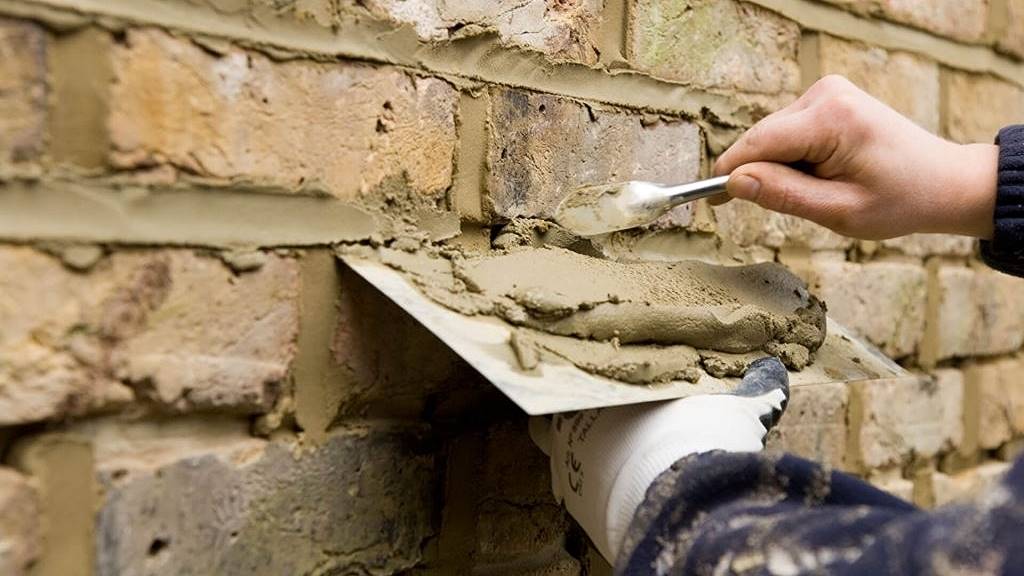 A hand applying mortar in brick repointing process