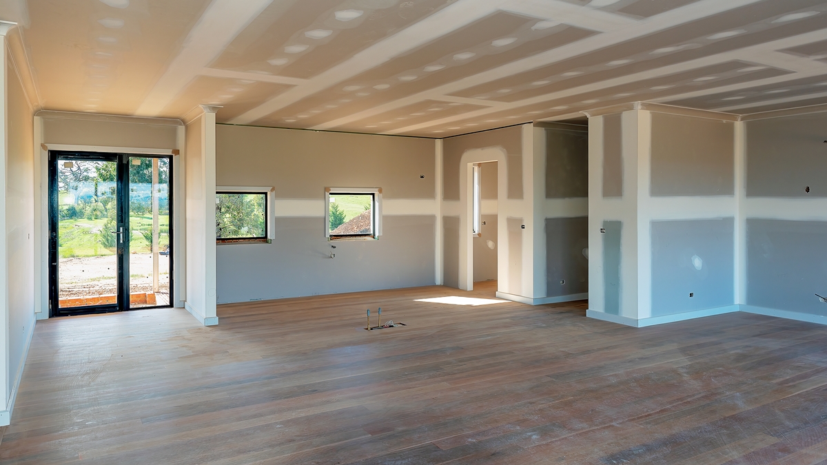 Interior of a new construction with unfinished dry lining, showing plasterboard walls and ceiling with visible joints and screw marks, ready for finishing.