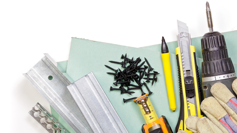 Selection of drywall installation tools including screws, metal channels, utility knives, and plasterboard.