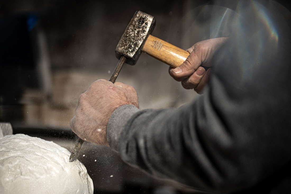 Stone mason carving stone with chisel and hammer for masonry work