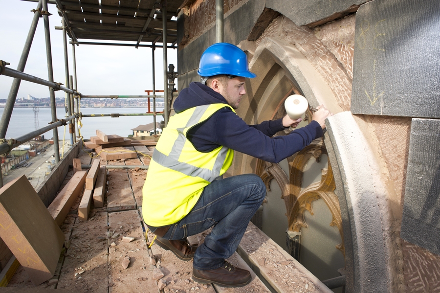 Stone mason performing repair work on archway stonework at height