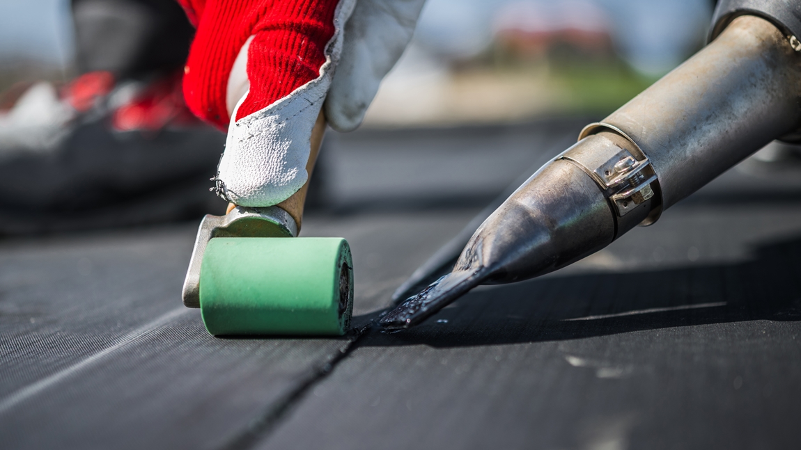 Close-up of EPDM rubber roofing membrane installation using a heat-welding tool and roller for a durable seal.