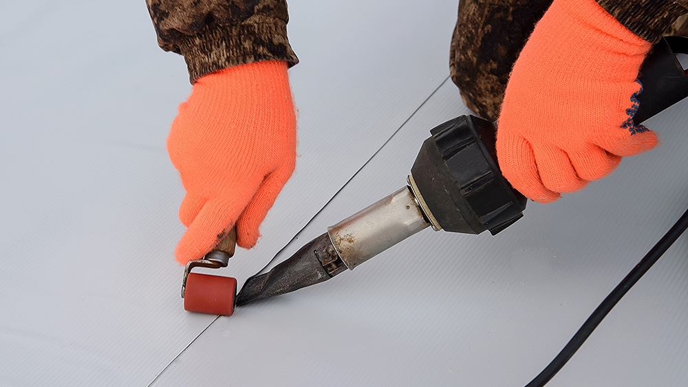 Installing TPO membrane using heat-welding tools for durable flat roof sealing.