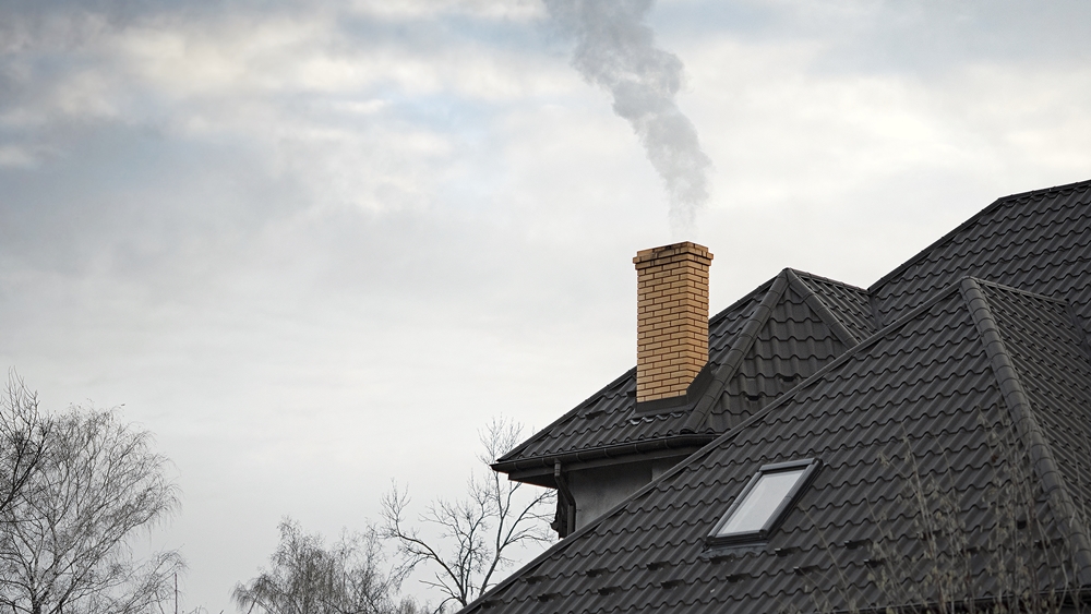Brick chimney stack on a tiled roof with smoke venting safely into the sky.