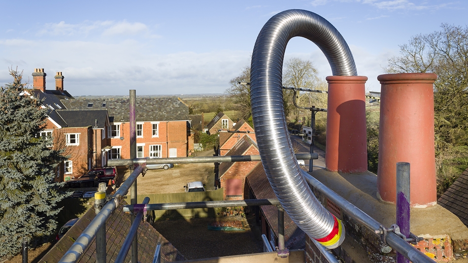Flexible stainless steel flue liner looped above chimney pots, being installed from secure roof scaffolding.