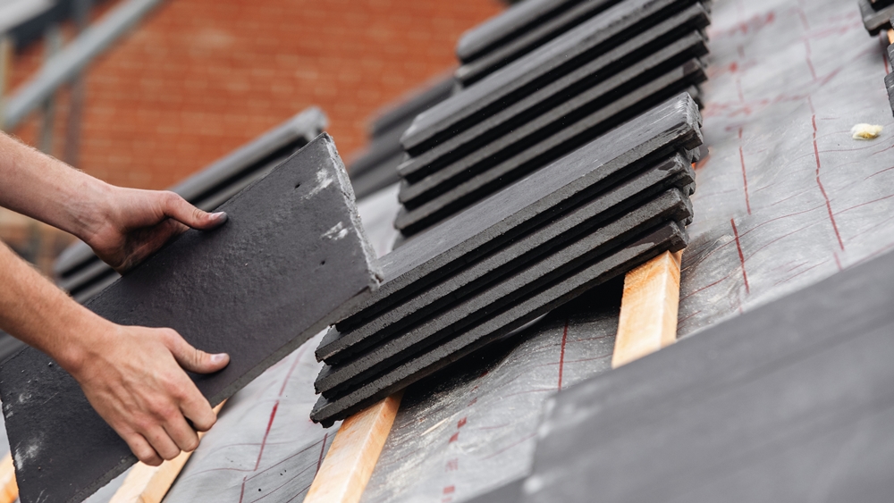 Worker stacking roof tiles on a pitched roof ready for installation