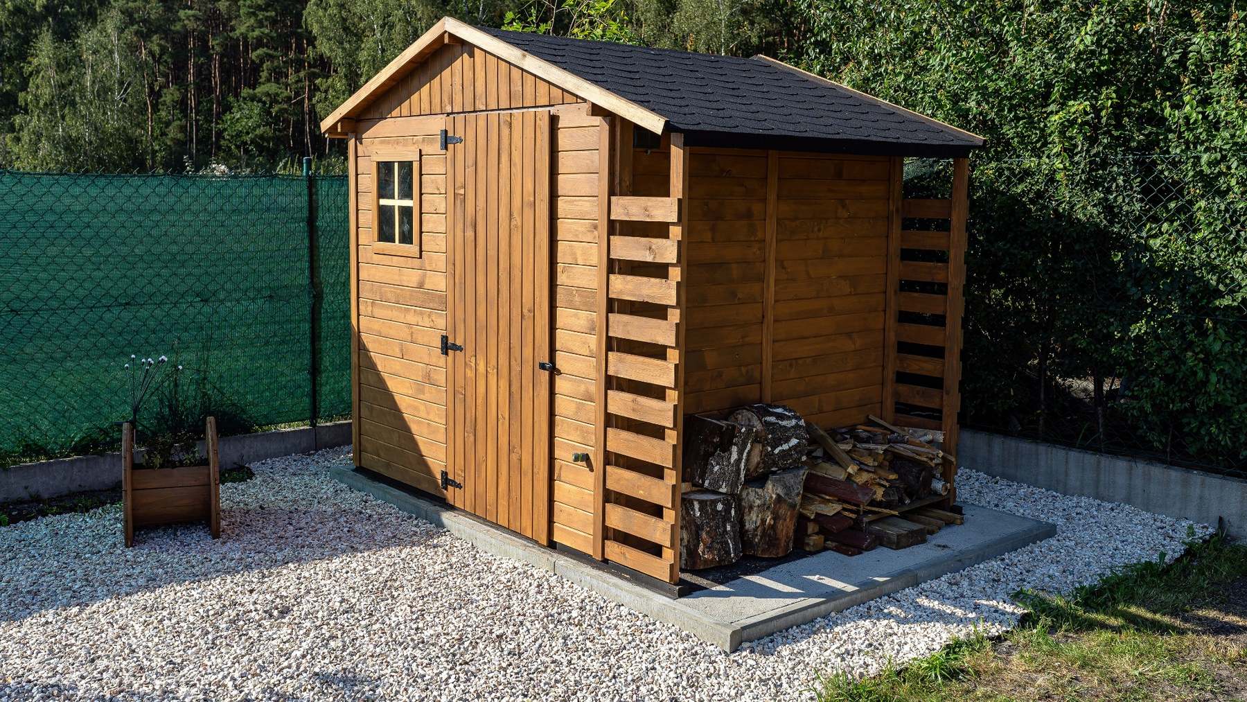 Timber garden shed and log store on a concrete base surrounded by gravel