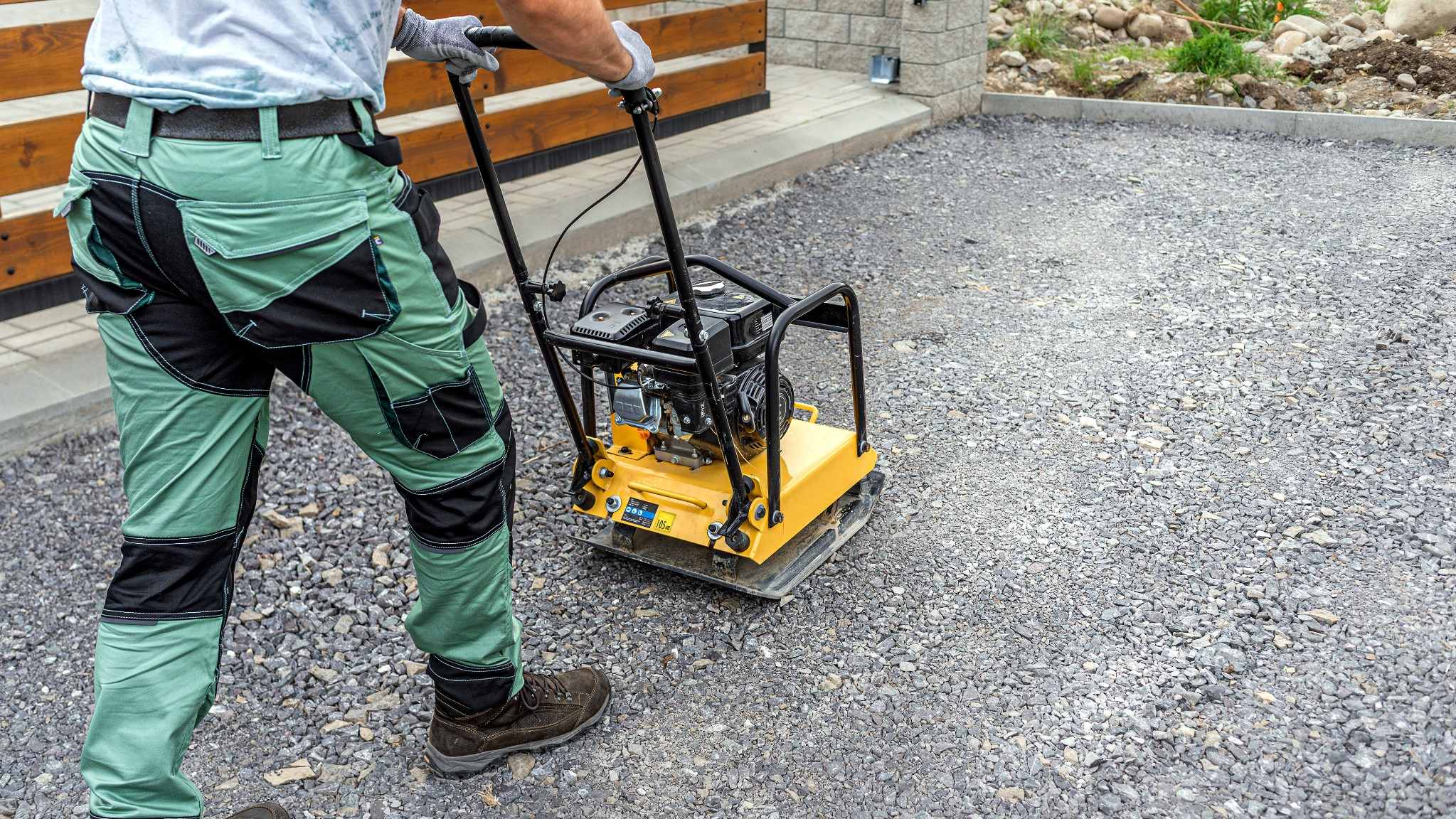Worker using a plate compactor to consolidate crushed aggregate for a sub-base