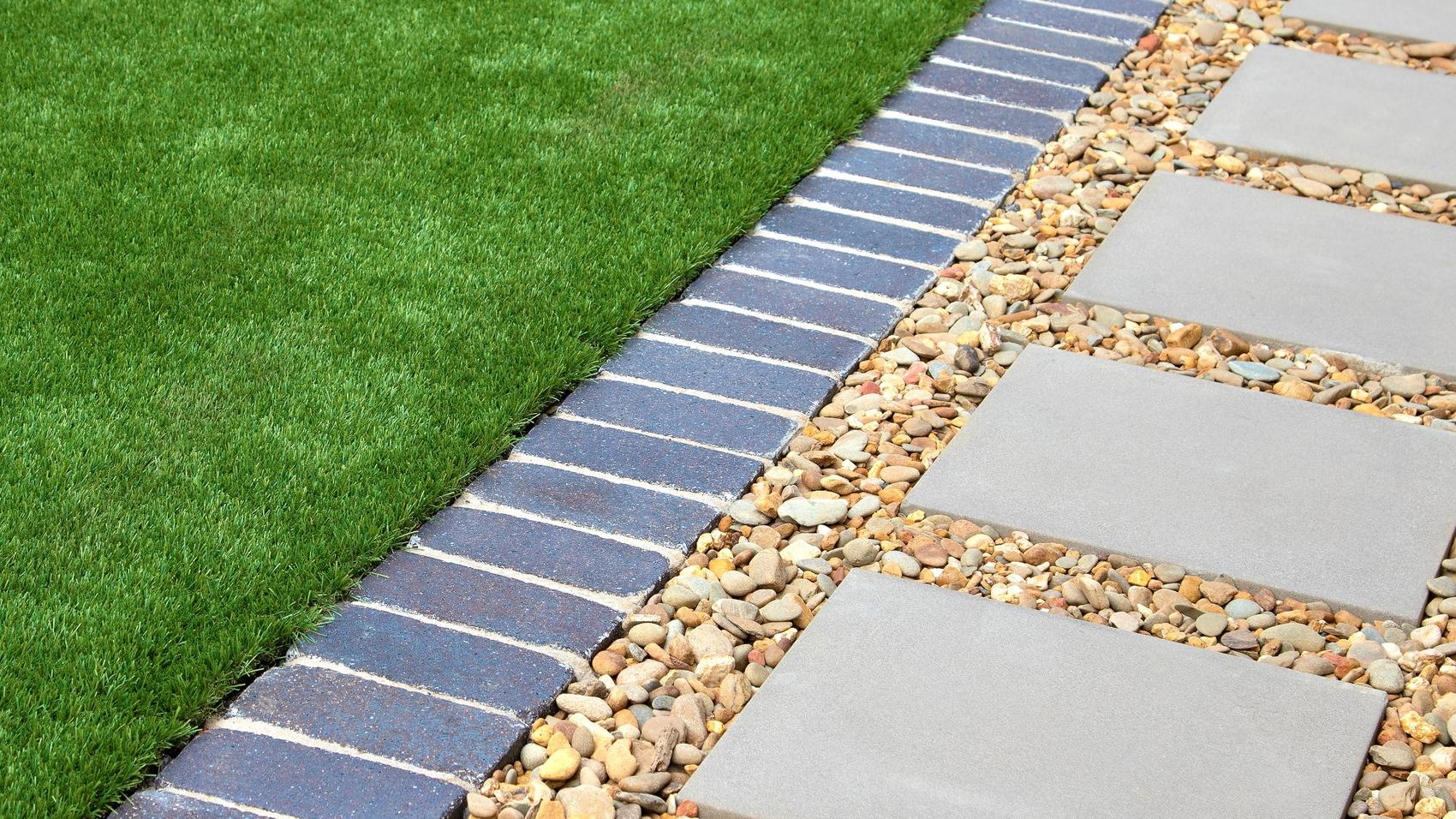 Stepping slabs in decorative gravel beside a grassed area and brick edging